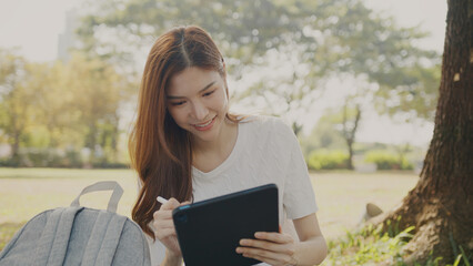 Obraz premium Attractive Freelance Woman Relaxing and Working Remotely in Nature, Happy Female Professional on a Video Call, Tech-Savvy Female Learning Online. Young Woman Reading and Communicating a Tablet