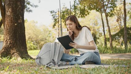 Fototapeta premium Asian Woman Working outdoors in the park. Professional on a Video Call, exploring Hybrid Work Opportunities in a Peaceful, Virtual Meeting and Online Learning. Hybrid work lifestyle concept by tablet