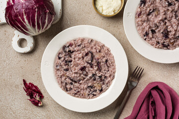 Italian risotto with round radicchio rosso and cheese in a white plate. Raw whole vegetable on a wooden board, ingredients. Beige table. Top view..