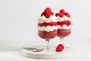Red Velvet Trifle, layers of red velvet cake, mascarpone cheese cream, berry jelly, fresh  raspberries served in a glass. On a white table and background.