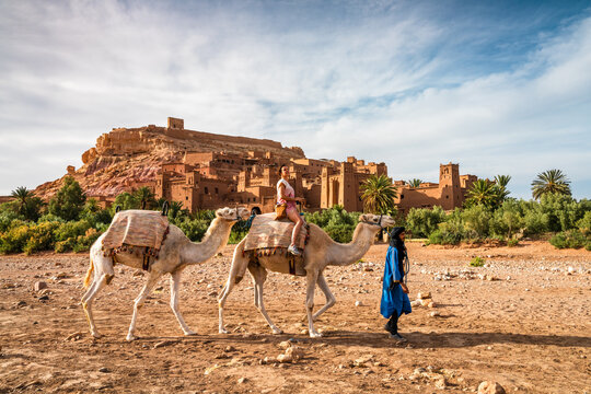 Woman riding a camel in front of old fortified town, Ait Benhaddou, Morocco