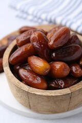 Tasty dried dates in wooden bowl on white table, closeup