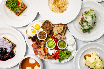 A vibrant breakfast spread featuring various dishes: poached eggs, toast, meats, fresh vegetables, and colorful garnishes, all presented on white plates, ideal for food-related themes.