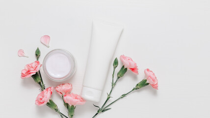 Bottle of facial cream with gentle pink flowers on white background top view. Skincare mockup bottle, cute feminine concept