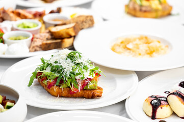 A close-up of a delicious croissant topped with fresh greens, tomatoes, and cheese, surrounded by an array of gourmet dishes. Perfect for food-related themes and culinary presentations.