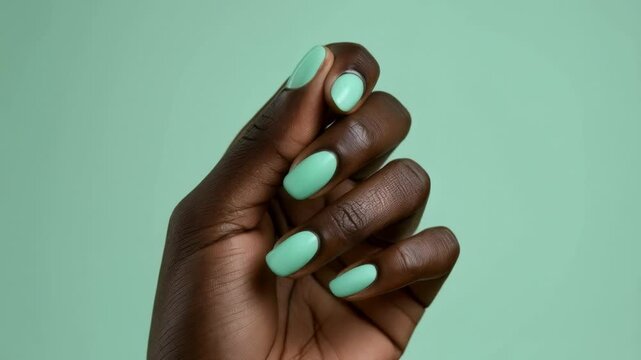 A close-up of a hand with perfectly polished mint green nails against a soft matching green background
