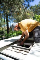Technician installing camper van roof vent under pine tree