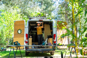 Carpenter installing campervan ceiling light in forest setting © Arianne