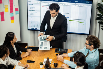 Project manager planning schedules for business task at meeting room, Gantt chart software show on TV screen. Multi ethnic diversity business people and modern business project management. Meticulous