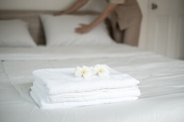 plumeria flower and towels on the bed in the luxury hotel room ready for tourist travel and Hands of the hotel maid clean the bedroom