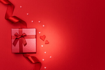 Red ribbon, red gift and small red hearts on red background. Happy Valentines day, Mothers day, birthday, wedding concept. Romantic flat lay.