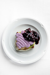 A delectable dessert featuring layers of creamy frosting in purple, topped with a rich berry compote. Presented elegantly on a white plate, perfect for showcasing culinary artistry.