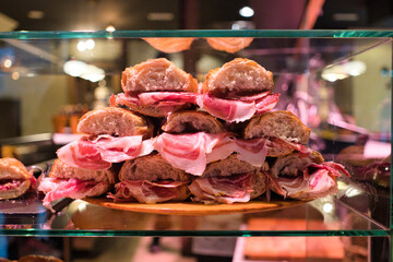 Several sandwiches made with crusty bread and filled with cured iberian ham are stacked on a wooden...