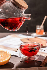 drops of red tea, woman pouring tea into a glass cup, hibiscus, tea with red berries, vitamin drink, winter tea for colds, lemon, red currant, black currant, raspberry, honey, cinnamon, anise
