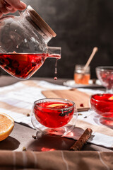 drops of red tea, woman pouring tea into a glass cup, hibiscus, tea with red berries, vitamin drink, winter tea for colds, lemon, red currant, black currant, raspberry, honey, cinnamon, anise