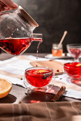 drops of red tea, woman pouring tea into a glass cup, hibiscus, tea with red berries, vitamin drink, winter tea for colds, lemon, red currant, black currant, raspberry, honey, cinnamon, anise