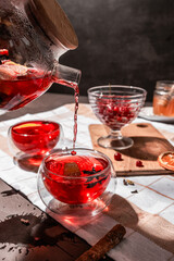 drops of red tea, woman pouring tea into a glass cup, hibiscus, tea with red berries, vitamin drink, winter tea for colds, lemon, red currant, black currant, raspberry, honey, cinnamon, anise