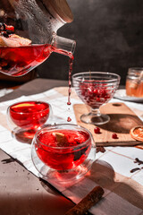 drops of red tea, woman pouring tea into a glass cup, hibiscus, tea with red berries, vitamin drink, winter tea for colds, lemon, red currant, black currant, raspberry, honey, cinnamon, anise