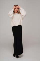 Trendy, fashionable woman posing in warm sweater, elegant maxi skirt and high heels, studio background.