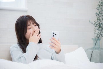 Young woman operating a smartphone in bed absentmindedly in bed in the morning.