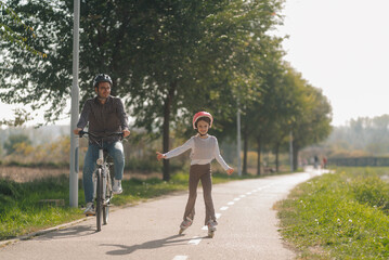 Fototapeta premium Father and daughter enjoying roller skating and cycling in a park