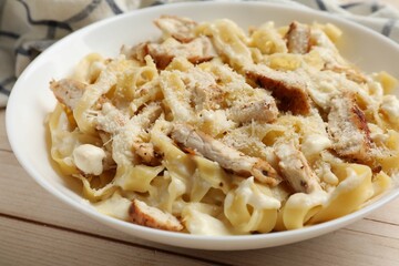 Tasty Alfredo pasta with chicken on light wooden table, closeup
