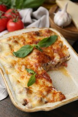 Delicious cooked lasagna with basil in baking dish on wooden table, closeup