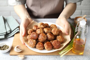 Woman holding plate with delicious meatballs at light textured table, closeup
