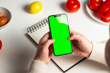 Planning healthy menu concept. Smartphone with green screen in hands. Calculating calories. Nutrients counting. Calorie tracking app mock up.