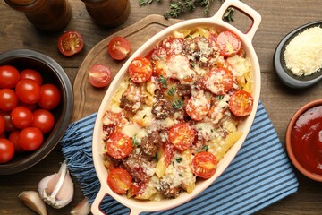Delicious pasta casserole in baking dish with ingredients on wooden table, flat lay
