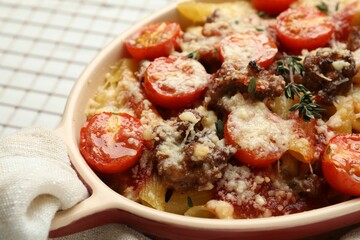 Delicious pasta casserole with cheese, tomatoes, minced meat and thyme in baking dish on white table, closeup