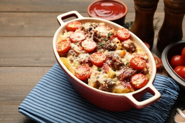 Delicious pasta casserole with cheese, tomatoes, minced meat and thyme in baking dish on wooden table, closeup