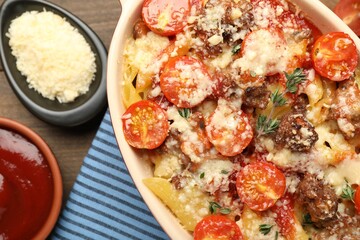 Delicious pasta casserole with cheese, tomatoes, minced meat and thyme in baking dish on wooden table, flat lay