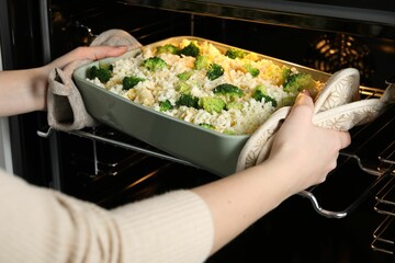 Woman putting dish with uncooked pasta casserole into oven indoors, closeup