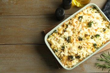 Tasty pasta casserole with cheese and broccoli in baking dish on wooden table, flat lay. Space for text