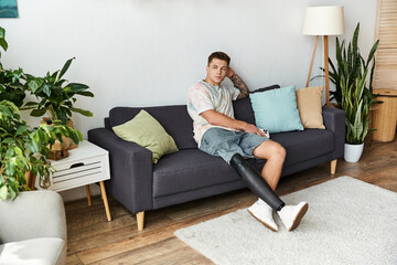 Young man relaxes on a cozy sofa with a prosthetic leg in a modern living space