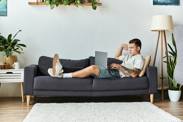 Young man with a prosthetic leg relaxes on a couch while working on a laptop at home