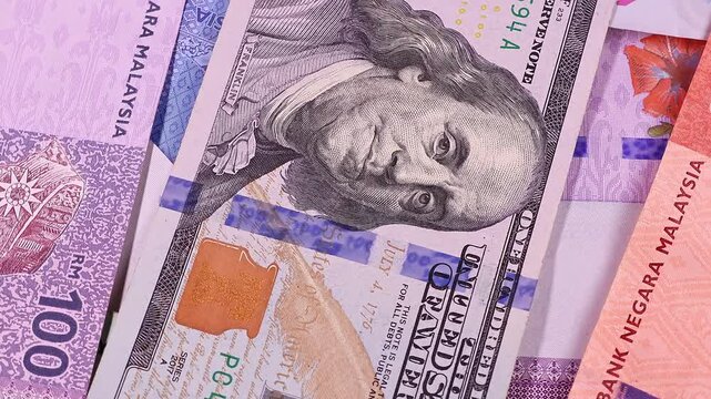 Close up view of rotating Malaysian ringgit (MYR) and 100 USD american dollars, brand new banknotes. Selective focus. Money background.