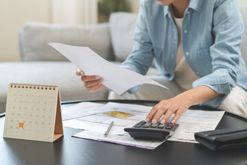 Stressed asian young business woman, employee using calculator to calculate expenses of monthly, hand holding bills and receipt for to payment on table at home. Financial, finance of banking concept.