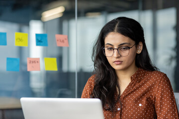 Serious thinking woman working with laptop inside office close up. Focused businesswoman reading...