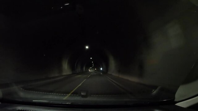Driving through a dark tunnel with ceiling lights. The vehicle moves smoothly along the road, immersed in the tunnel's dimly lit atmosphere.