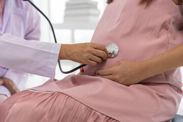 Female senior doctor use stethoscope listening sound of baby in pregnant belly