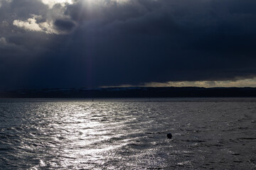 Obraz premium Single person in silhouette walking around coastal marine lake in dark and stormy weather conditions