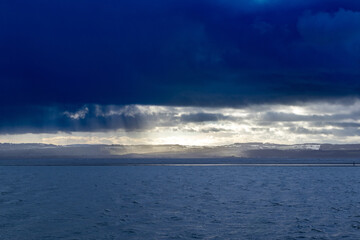 Single person in silhouette walking around coastal marine lake in dark and stormy weather conditions
