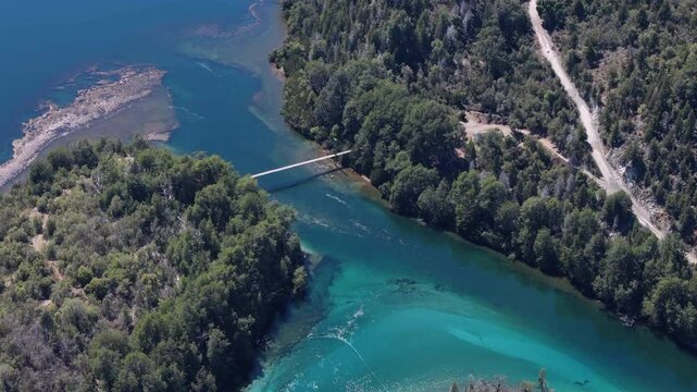 Aerial Shot of Suspension Bridge Amid Pristine Forest and Clear Waters in Patagonia, Argentina.