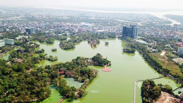 A stunning aerial perspective of Kandawgyi Lake in Rangun, Myanmar, showcasing its lush green surroundings, small islands, and the vibrant cityscape in the background