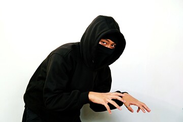 A person in a black hoodie and face mask posing with mysterious hand gestures. The photo captures a...