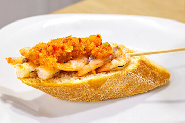 Traditional pintxo from San Sebastian: Grilled prawn tails served on bread and topped with a vinaigrette of red pepper, green pepper, and chive.