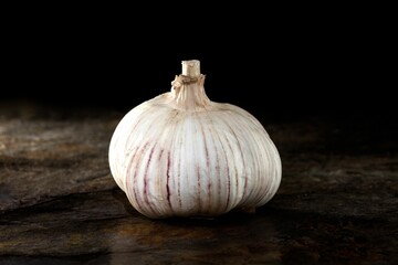 A close-up shot of a single garlic bulb on a dark rustic surface.