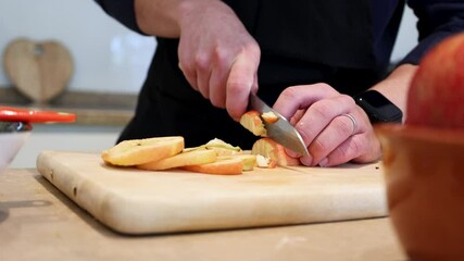 Close up of man cutting fresh apples with a knife on a wooden board preparing a homemade dessert, concept of cooking, healthy food, kitchen lifestyle, and domestic culinary preparation